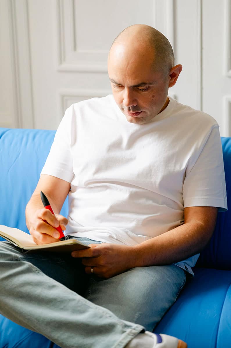 portrait designer graphique Charles Trombetta, assis dur divan bleu Klein dans un studio